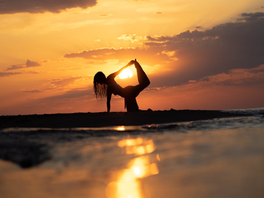 A woman in a peaceful yoga pose outdoors near calm water during sunset.
